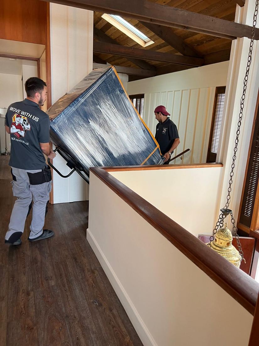 Mover guiding a blanket-wrapped dresser on a dolly toward the stairs